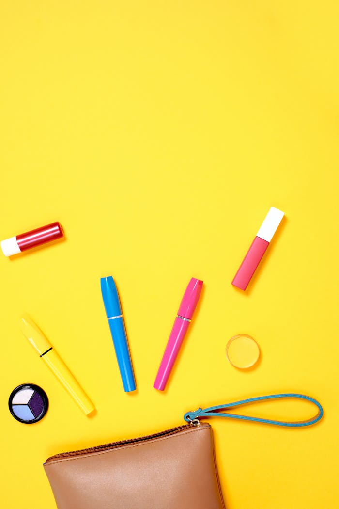 Flatlay of assorted colorful cosmetics with ample copy space on a bright yellow background.